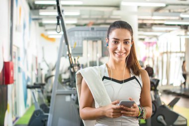 Gülümseyen kız spor salonunda akıllı telefonda en sevdiği şarkıları dinliyor..