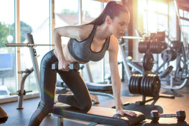 Spor giyimli genç, zayıf bir kadın spor salonunda ağırlık çalışıyor.