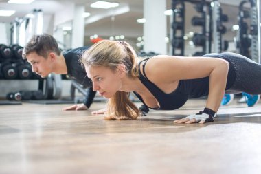 Sportif genç kadın ve erkek spor salonunda birlikte şınav çekiyorlar..