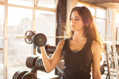 Spor salonunda ağırlığı olan genç bir kadının portresi.