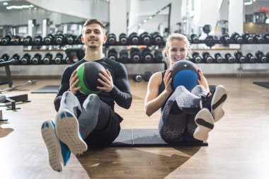 Spor yapan çift spor salonunda spor toplarıyla karın egzersizi yapıyor..