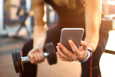 Cep telefonu ve spor salonunda ağırlığı olan tanınmamış bir kadın. Kapat..