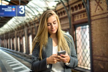 Tren istasyonunda telefonu kullanan güzel sarı saçlı genç bir kadının portresi..