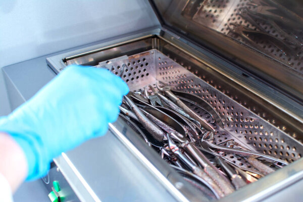 Close up of dentists hands taking out sterilizing medical instruments from autoclave