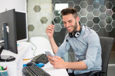 Ofis masasında telefonu kullanan yakışıklı güler yüzlü bir iş adamı.