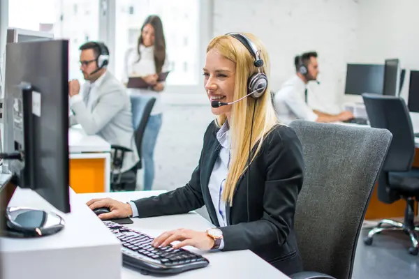 Ofiste meslektaşları olan bilgisayar kullanan kadın müşteri hizmetleri temsilcisi