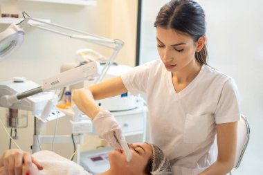 Güzellik uzmanı spa salonundaki genç bir kadının yüzüne modern aletlerle yüz bakımı uyguluyor.