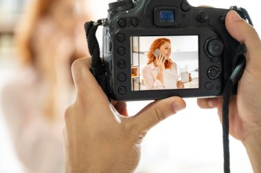 Erkek ellerinin profesyonel bir DSLR kamerasını tutarken ve genç kızıl saçlı kadının fotoğrafını çekerken. İçerde Fotoğraf Çekme.