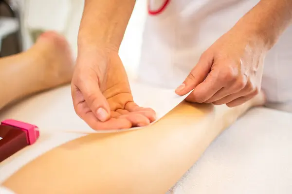 Close-up of a beautician waxing leg of woman with wax strip at a beauty spa.