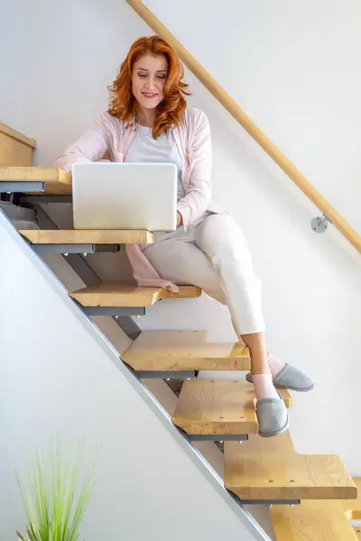 坐在楼梯上 在笔记本电脑上工作的姜汁女青年的照片 — 图库照片