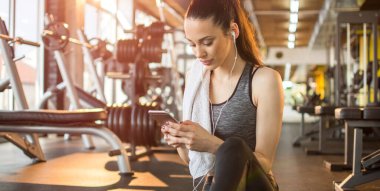 Paspasın üzerinde oturan ve spor salonunda cep telefonu kullanan genç bayan sporcu.