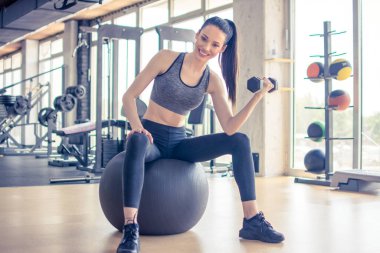 Spor salonunda spor salonunda spor yaparken dambıllarla spor yapan genç bir kadın.