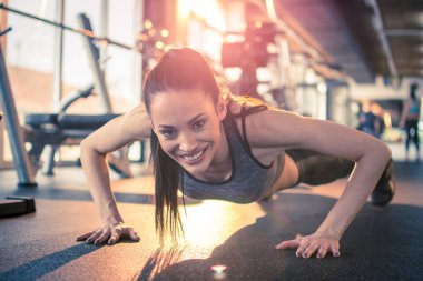 Fitness 'li genç bir kadın şınav çekiyor ve spor salonunda kameraya bakıyor. Cana yakın, çekici bir kız sabah spor salonunda gün ışığında şınav çekiyor..