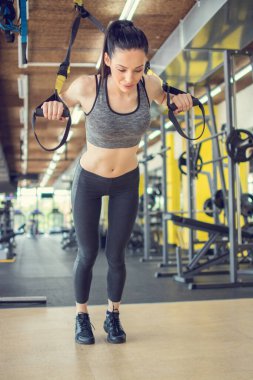 Spor salonunda süspansiyon kayışlarıyla TRX egzersizleri yapan sportif bir kadın. Çekici, zayıf, formda bir kadın sabah antrenmanı sırasında süspansiyon kayışlarıyla çalışıyor..