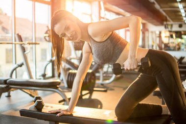 Spor giyim sektöründe spor salonundaki spor salonundaki spor salonunda ağırlık kaldıran genç bir kadın. Çekici, güler yüzlü bir kız. Sabahları gün ışığının önünde çalışıyor..