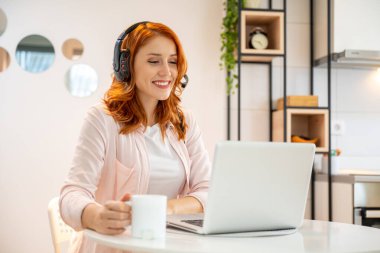 Genç mutlu kızıl kız kahve içerken çağrı merkezinde ajan olarak çalışıyor. Kulaklık takmak ve dizüstü bilgisayarda yazmak..