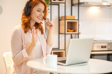 Genç gülümseyen kızıl saçlı çağrı merkezi ajanı kafasında kulaklığı olan müşteriye el sallıyor ve bilgisayarında video görüşmesi yapıyor. Günlük kıyafetler giyip, kahve içiyorlar..