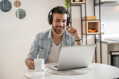 Keyfi yerinde genç bir adam evden kahve içerken çağrı merkezinde ajan olarak çalışıyor. Kulaklık takmak ve dizüstü bilgisayar kullanmak..