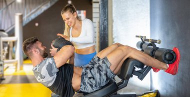 Spor salonunda spor salonunda spor yaparken kas sporcusuna yardımcı olan bayan kişisel antrenör spor salonunda spor salonunda spor topuyla şınav çekiyor..
