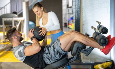 Spor salonunda spor salonunda spor yaparken kas sporcusuna yardımcı olan bayan kişisel antrenör spor salonunda spor salonunda spor topuyla şınav çekiyor..