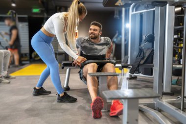 Yakışıklı, kaslı bir adam spor salonunda sarışın seksi bir kızın yardımıyla ağır tabakla egzersiz yapıyor..