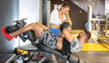 Genç bayan kişisel antrenör spor salonunda spor salonunda spor yaparken kaslı bir adama yardımcı oluyor..