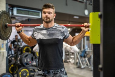 Yakışıklı kaslı adam spor salonunda ağırlık kaldırıyor.