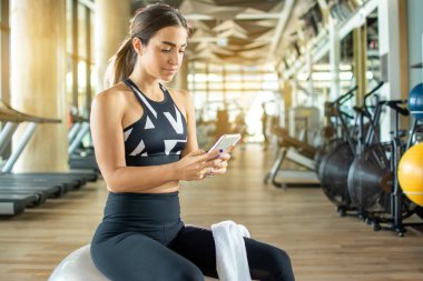 Spor giyinen güzel bir kadın spor salonundaki spor eğitiminden sonra akıllı telefon kullanıyor.