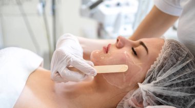 Beautician applying hydro gel mask on the young woman face, before laser treatment in beauty salon. Close up side view.