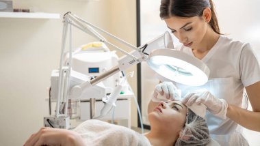 Kozmetik uzmanı kadın hastaların alnına sivilce sıkıyor.