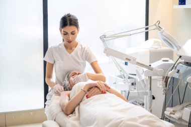 Güzellik uzmanı genç kadınların yüzüne jel maske takıyor. Güzellik salonunda lazer tedavisinden önce..