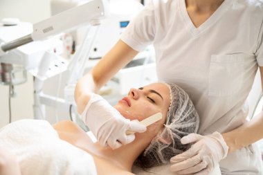 Güzellik uzmanı genç kadın yüzüne jel maske takıyor. Güzellik salonunda lazer tedavisinden önce..