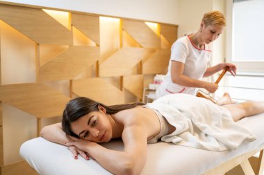 Selülit masajı yapan genç ve güzel bir kadın. Güzellik salonunda ahşap bir oklava takmış..