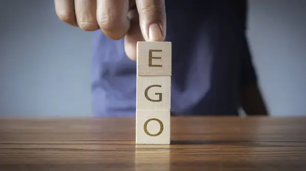 Ego on wooden alphabet blocks reading - Ego - balanced in the palm of his hand in a conceptual image