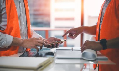 Mühendisler ya da ustabaşları akıllı telefon kullanan ve şantiyede güvenlik tişörtü giyen projeler üzerinde tartışıyorlar.
