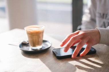 Sosyal medyayı akıllı telefonla kontrol etmek kafede kahve içmek güzel güneş ışığına karşı, rahatlatıcı bir an yaşamak