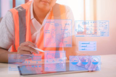 Kimyasal makine üretiminin sanal diyagramına sahip dijital tablet kullanan bir mühendis sabit başlıklı PPE ile bölge ofisindeki masada çalışıyor