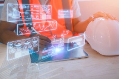 Kimyasal makine üretiminin sanal diyagramına sahip dijital tablet kullanan bir mühendis sabit başlıklı PPE ile bölge ofisindeki masada çalışıyor