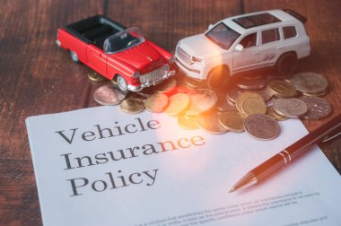 Araba sigortası oyuncak arabalarının araç sigortası yönetimi ve finansal planlama kavramında masaya kalem ve sikke yazarken seçici odak görüntüsü