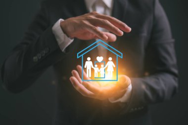 Ev ve Aile Sigortası Emlak Konsepti, iş adamı alıkoyma ve bir aile ve ev ikonunu karşılama. Emlak sigortası ve güvenlik kavramı