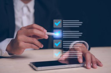 Kalite kontrol listesi geribildirim, kalite iyileştirme ve maliyet yönetimi stratejik planlama ve performans artırımı kavramında akıllı telefon ve kalem tiki doğru işaretini kullanan işadamı