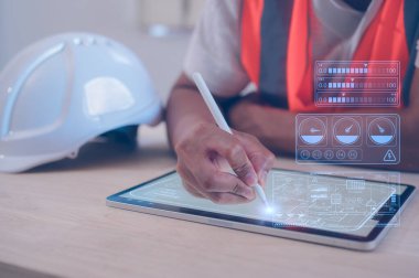 Turuncu yelek giyen mühendis ofis kaskı takıyor. Dijital tablet üzerinde çalışan kalem kullanıyor. Sanal ekran üzerinde veri analizi yapıyor.