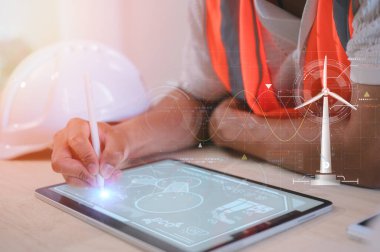 Turuncu yelek giyen mühendis ofis kaskı takıyor dijital tablet üzerinde çalışıyor sürdürülebilir iş ve enerji kavramında sanal ekrandaki veri grafiklerini analiz ediyor.