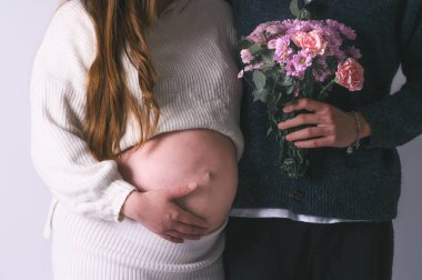 Hamile bir çiftin bebek karnına dokunduğunu ve tuttuğunu ve çiçekleri tuttuğunu yakın çekimde birkaç el hamile karnında, müstakbel anne ve babanın elleri hamile büyük karnında sıkıştı.