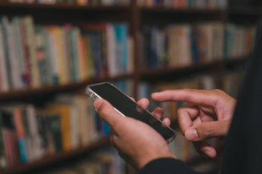 Sosyal medya pazarlama kavramı. Akıllı telefon yazma, sohbet kutusu simgelerindeki sohbet konuşmalarını kullanan erkek eli bulanık kitaplık arka planıyla ortaya çıkar