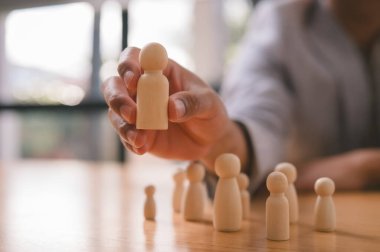 Bir iş adamının gruptan ahşap bir insan figürü seçmesi, işe alım, liderlik, yetenek seçimi, karar verme, İK, yönetim ve iş dünyasındaki bireyselliği sembolize ediyor.