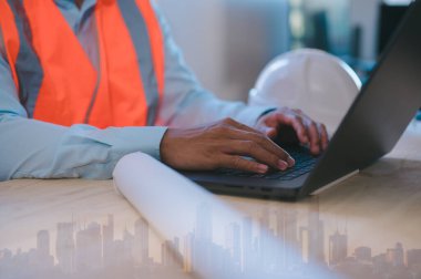 Şehir geçmişi bulanık bilgisayar kullanan bir mühendis, arka planda şehir binaları olan ofis masasında uzaktan çalışma teknolojisi kullanan bir ustabaşı.