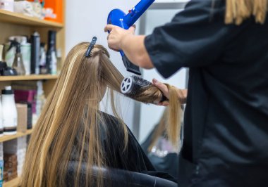 Professional hair styling session in a beauty salon with a hairdresser blow-drying a blonde client's long hair clipart