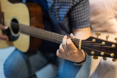 Gitar ensesine ip bağlayan bir adamın detaylı görüntüsü. Müzikal alıştırma ve tekniğin samimi çekimi, rahat bir ortamda kapalı bir yerde çekildi.
