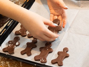 Önlüklü, çikolatalı kurabiye hamurunu unlu, dağınık bir tahta masada yoğuran bir çocuğun yakın çekimi. Ev yapımı pişirme ve elleriyle mutfak eğitimi.